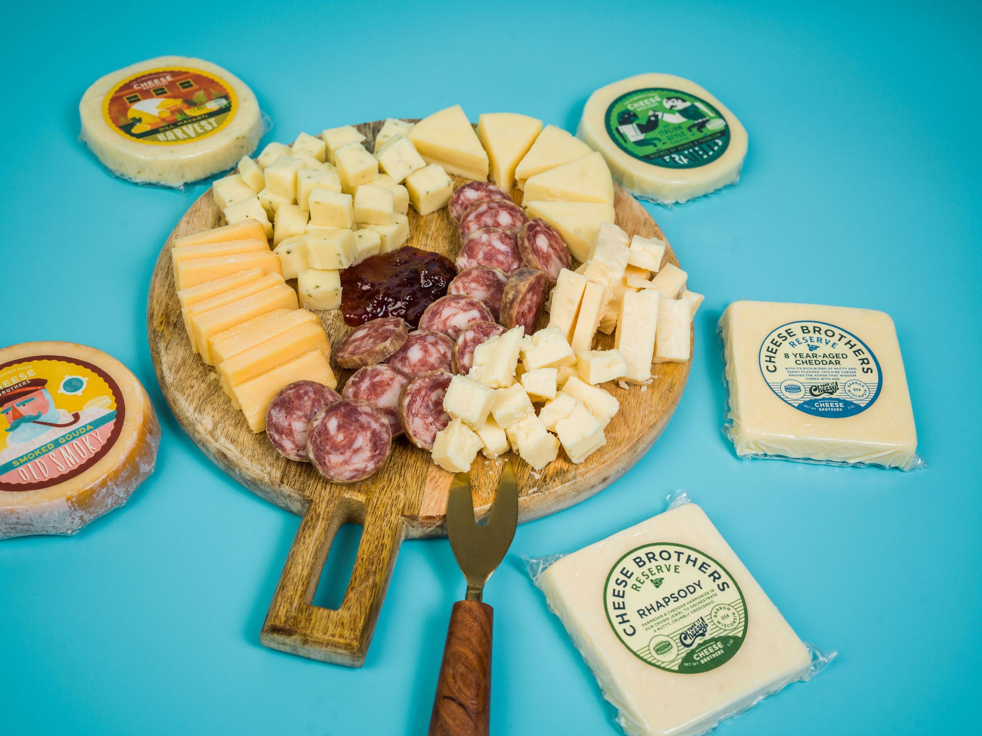Charcuterie board with jam, sausage, and five varieties of artisan Wisconsin cheeses with packaging. 
