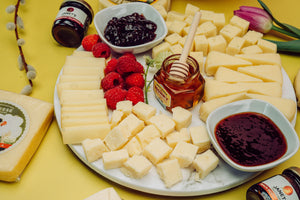 Mother's Day charcuterie board with a variety of gourmet cheeses, berries, jam, and honey. 