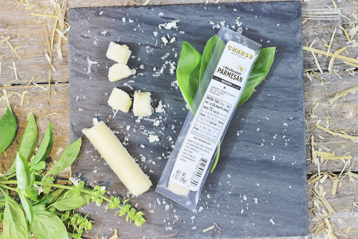 Parmesan gourmet cheese sticks in and outside the package on a black slate with herbs. 