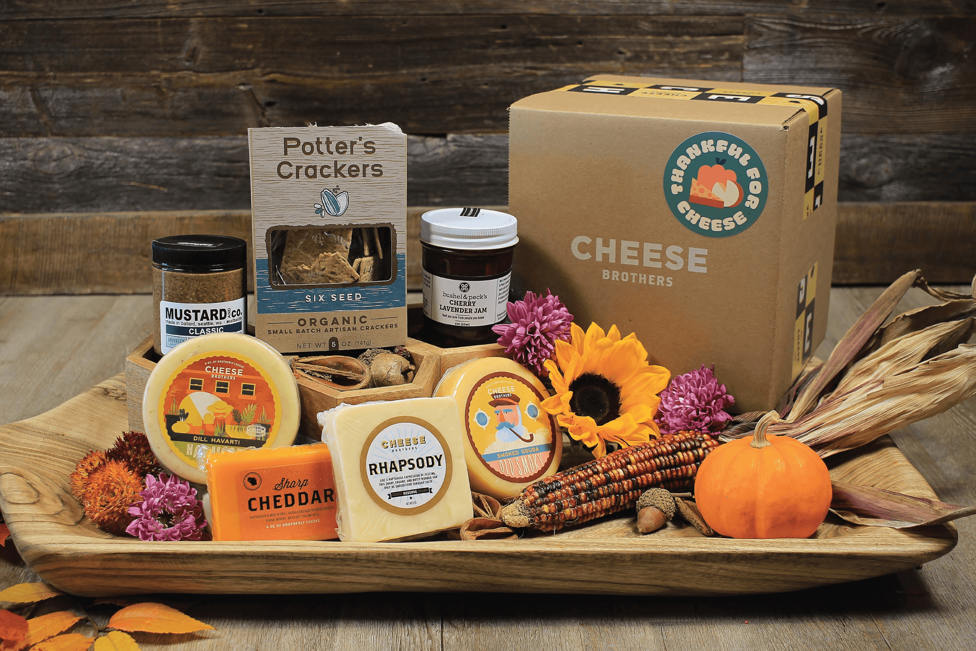 Thanksgiving cheese box with a variety of cheeses, jam, mustard, and crackers in a fall display. 