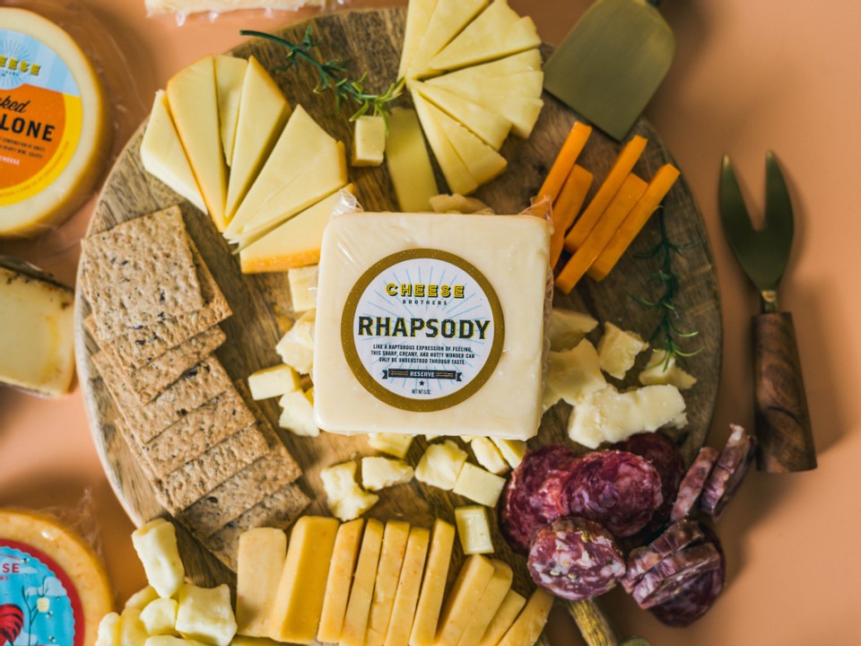 A package of rhapsody parmesan and cheddar cheese on a charcuterie board.