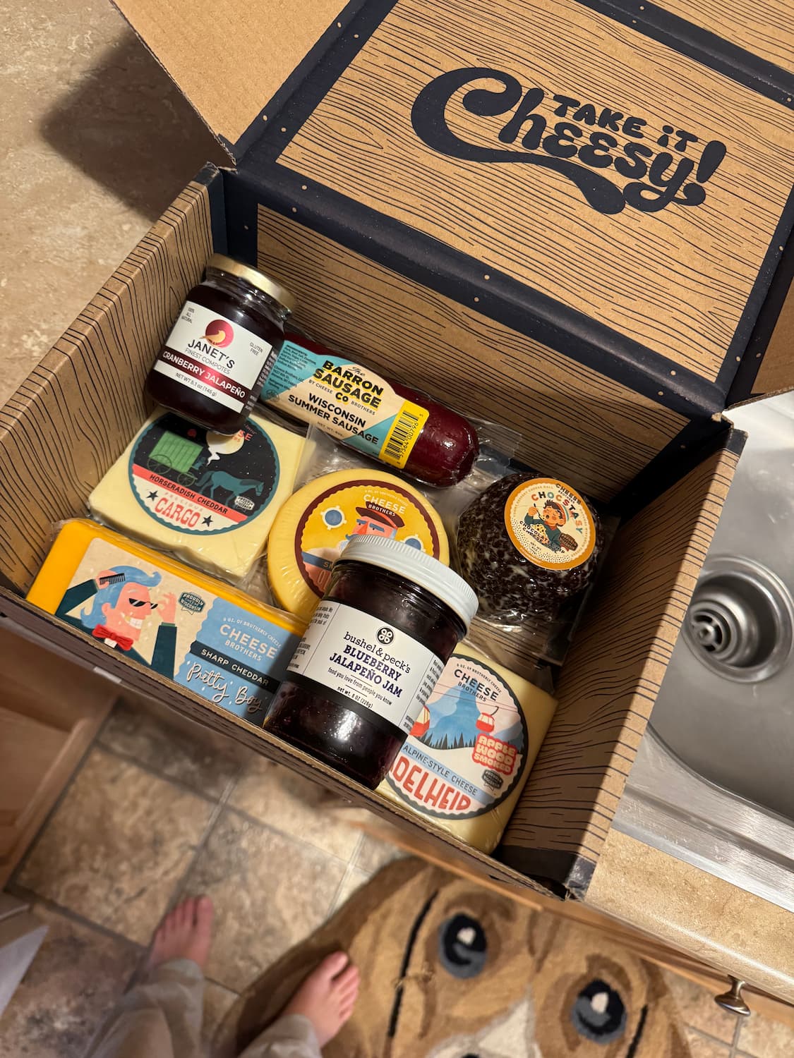 Open box labeled 'Take It Cheesy!' with various food items including cheese and condiments.