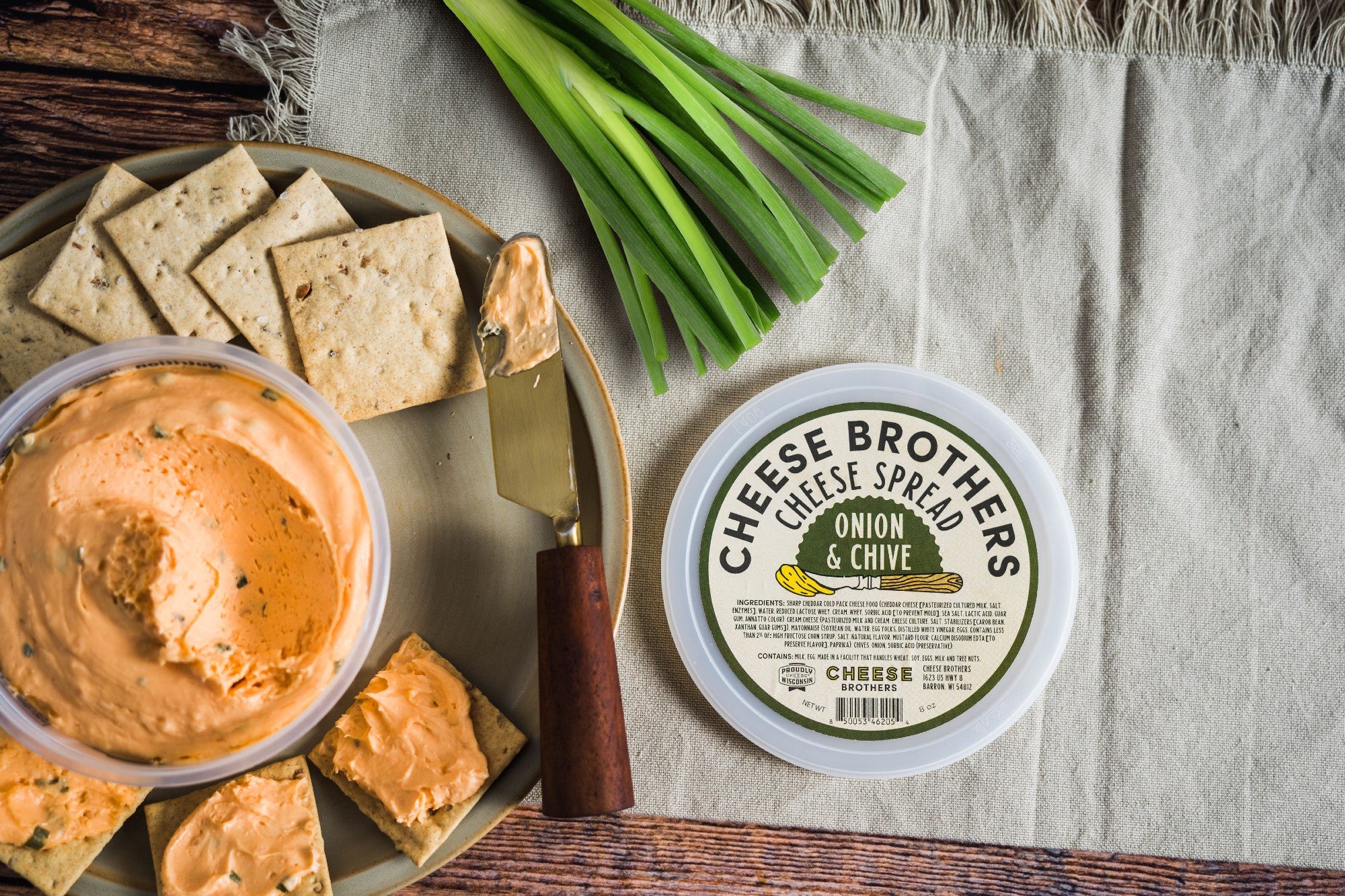 Container of onion and chive cheese spread with crackers and chives. 