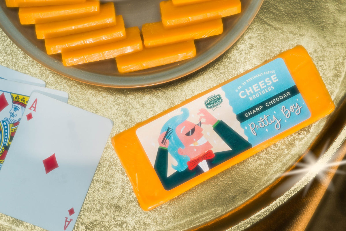 Block of Pretty Boy sharp artisan Wisconsin cheddar next to playing cards and cheese slices. 