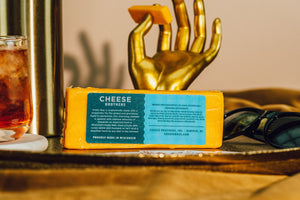 Zoomed in on the back of Pretty Boy sharp cheddar cheese with golden hand holding cheese slice. 