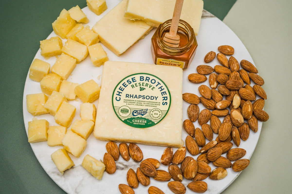 Package of Rhapsody parmesan and cheddar cheese on a charcuterie board with nuts, honey, and cheese cubes. 
