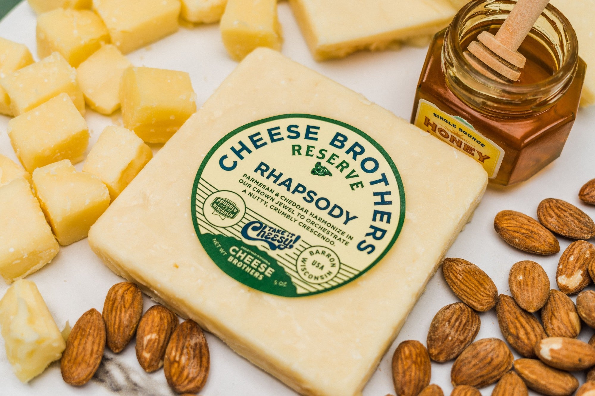 Package of Rhapsody  parmesan and cheddar cheese surrounded by nuts, honey, and cheese cubes. 