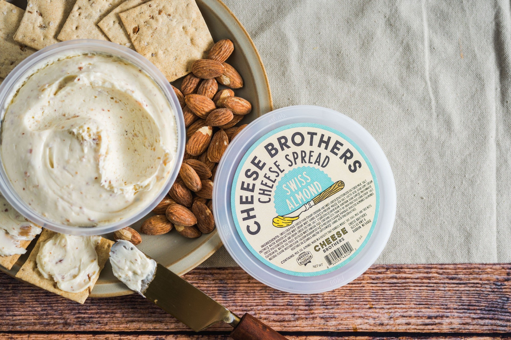 Container of Swiss Almond cheese spread next to crackers and nuts. 