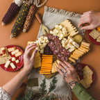 Cheese board with a selection of cheeses and dips with people helping themselves.