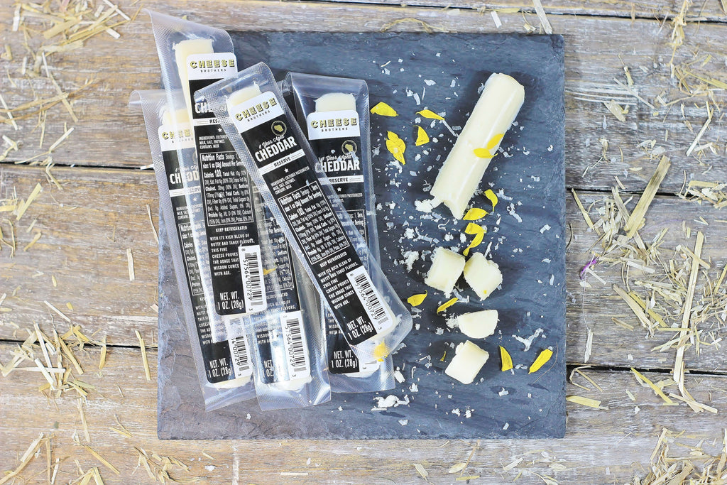 Black slate with packages of gourmet cheddar cheese sticks.