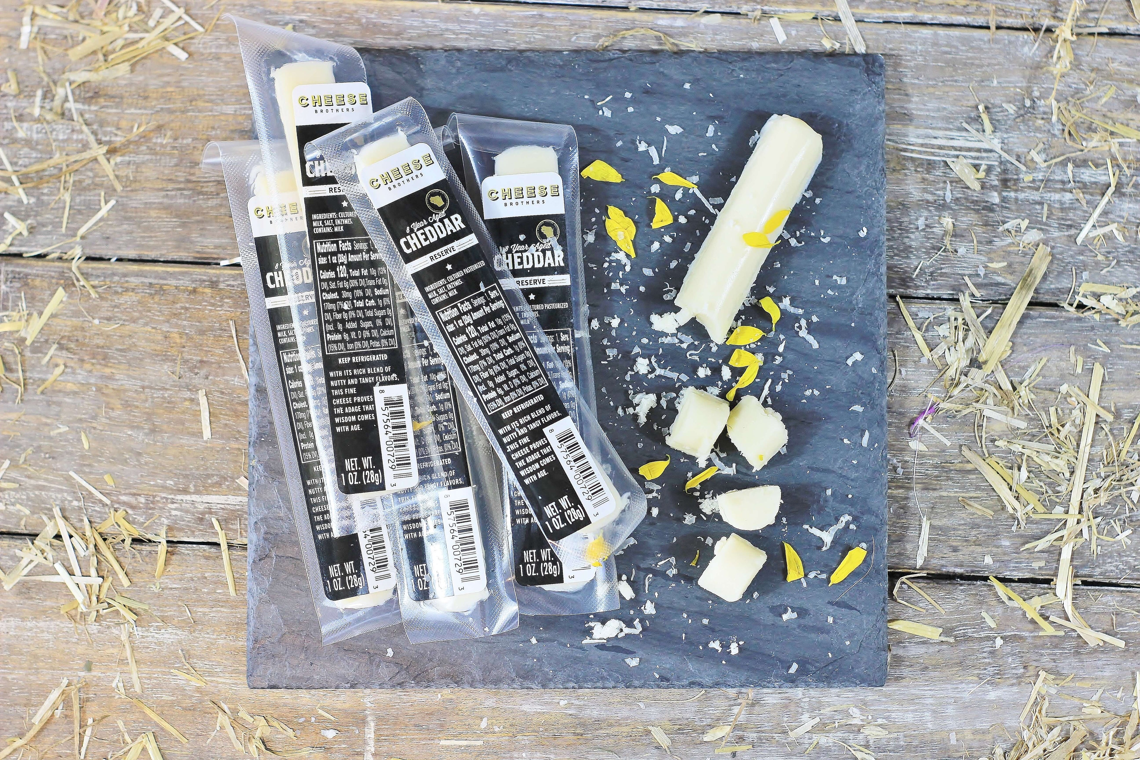 Black slate with packages of gourmet cheddar cheese sticks.