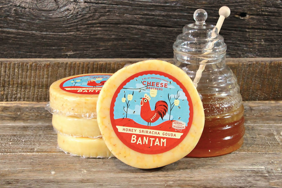 Package of Bantam Sriracha gouda in front of stacks of the same artisan cheese and a jar of honey. 