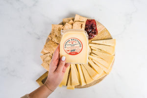 Hand holding a package of door county duet gouda parmesan cheese above charcuterie board. 