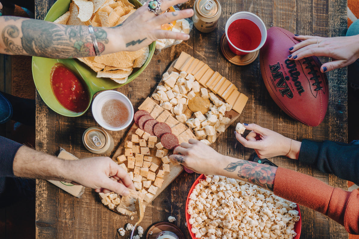 Friends sharing charcuterie board and other snacks during football game