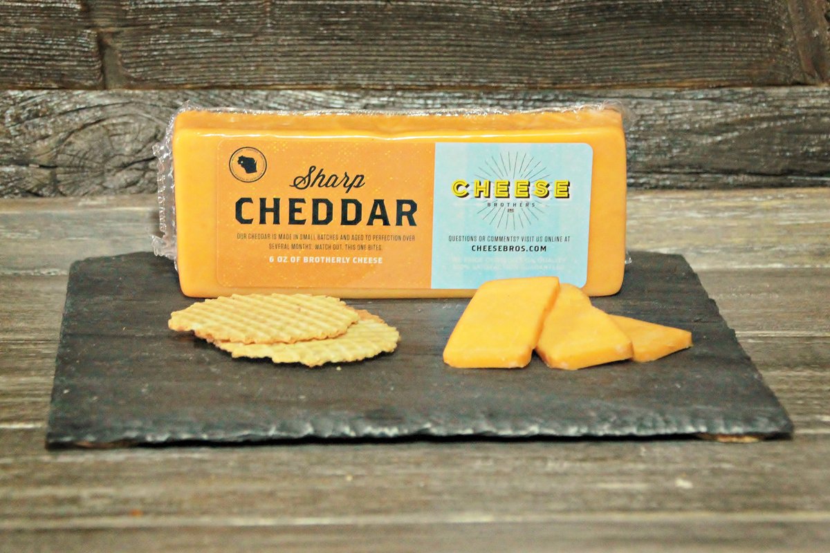 Block of Gourmet Sharp Wisconsin Cheddar with cheese slices and crackers on black slate. 