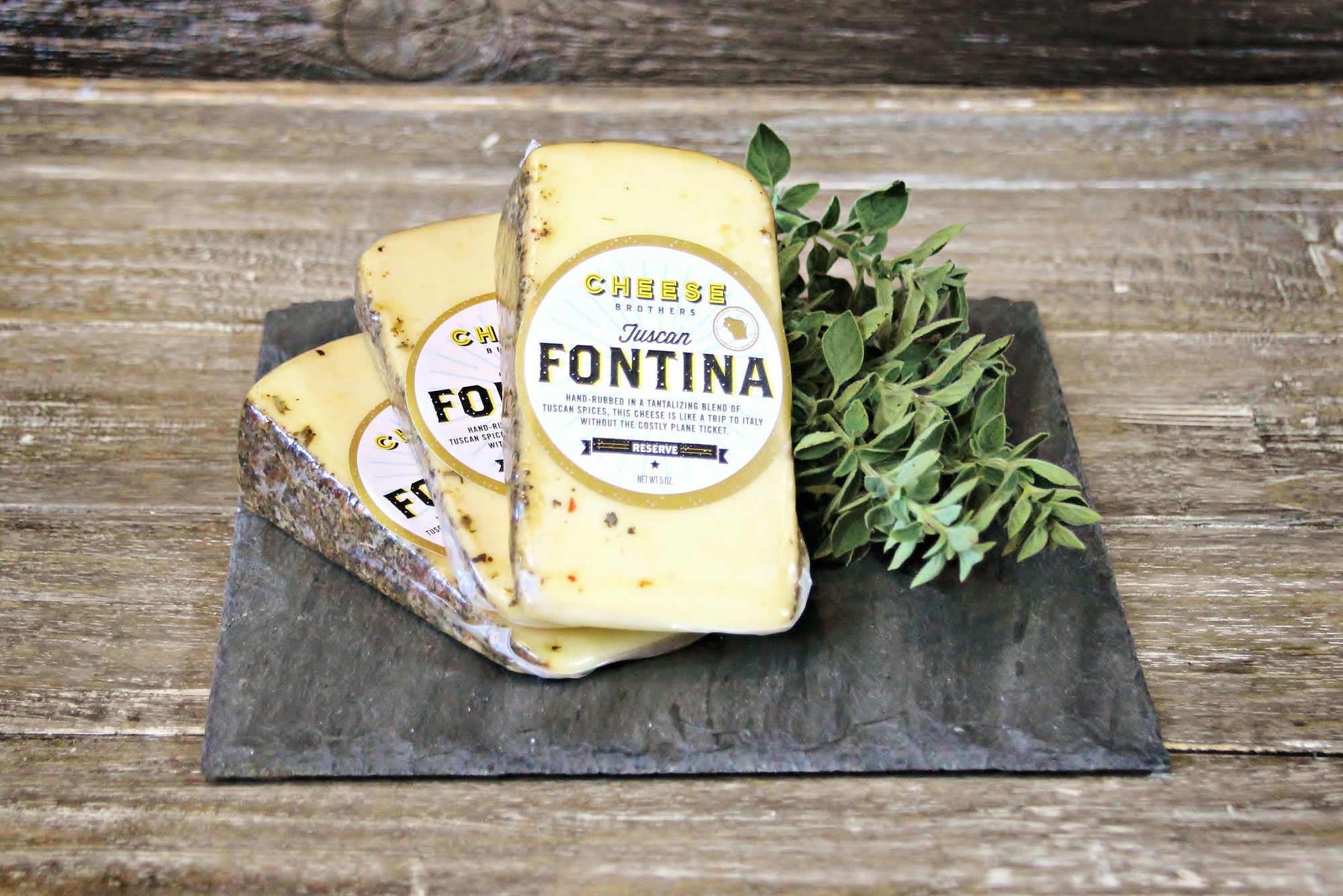 Three stacked packages of Cheese Brothers Fontina cheese on a black slate board.