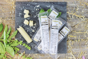 Parmesan gourmet cheese sticks in and outside the package on a black slate with herbs. 