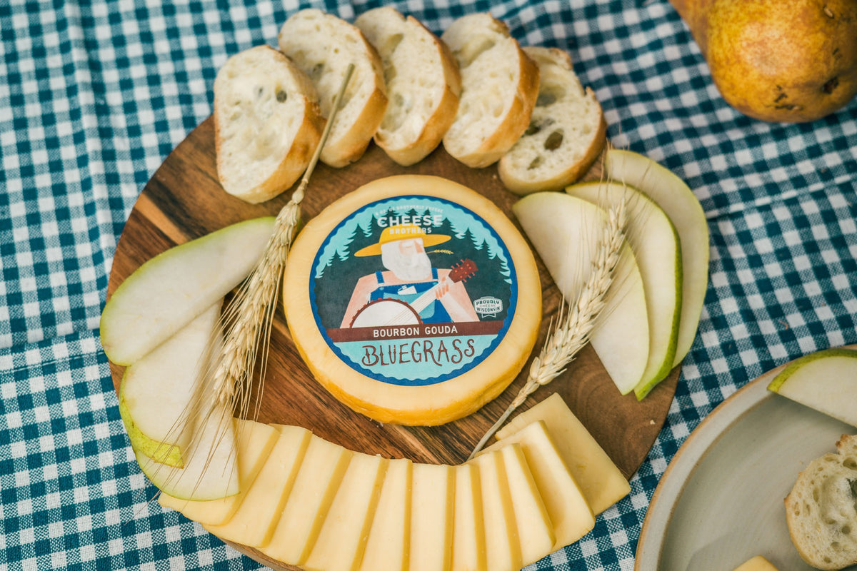 Package of Bluegrass bourbon gouda on board with bread, apples, and sliced cheese. 