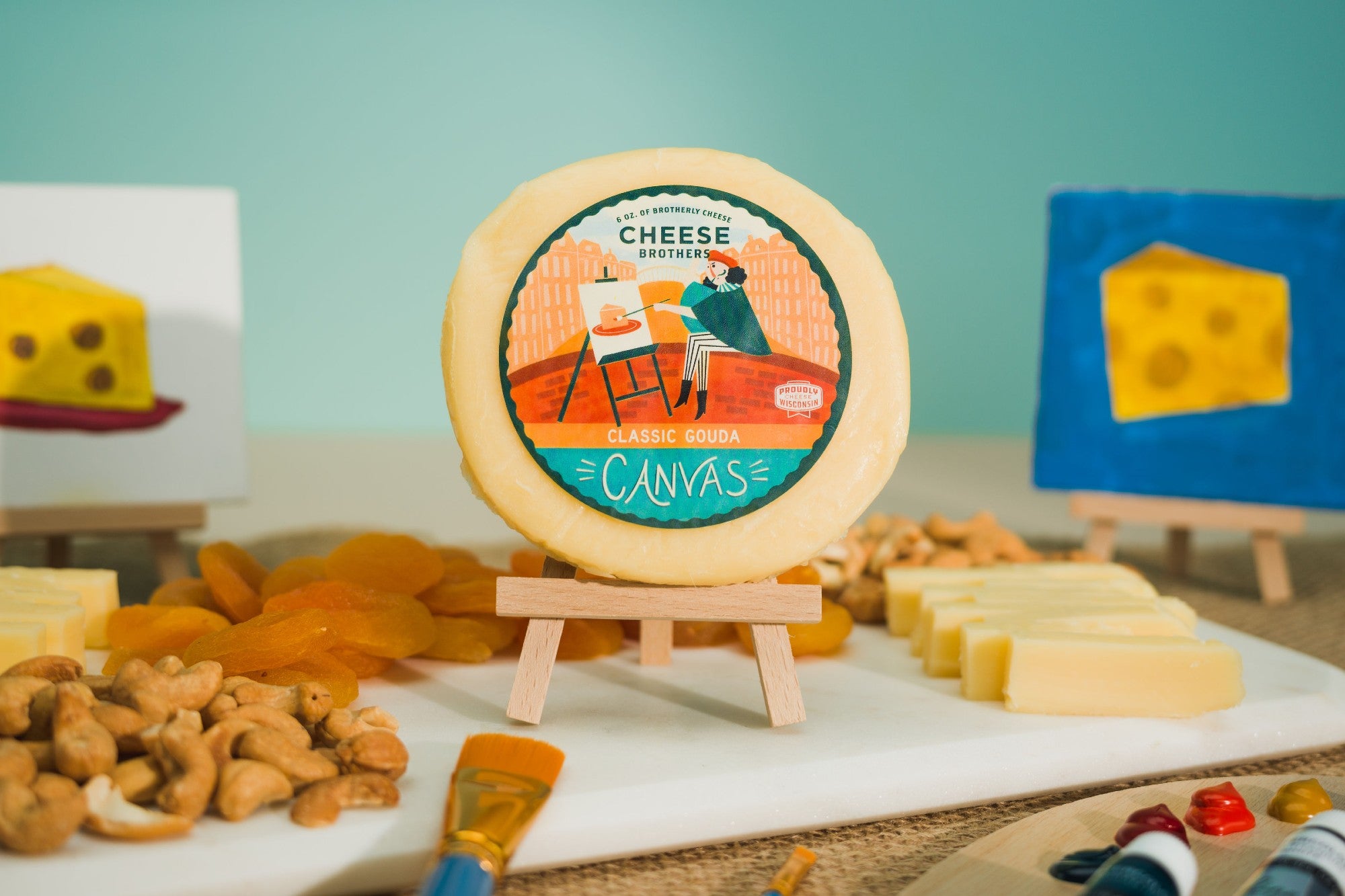Cheese Brothers canvas gouda cheese on art easel with charcuterie board in an art space. 