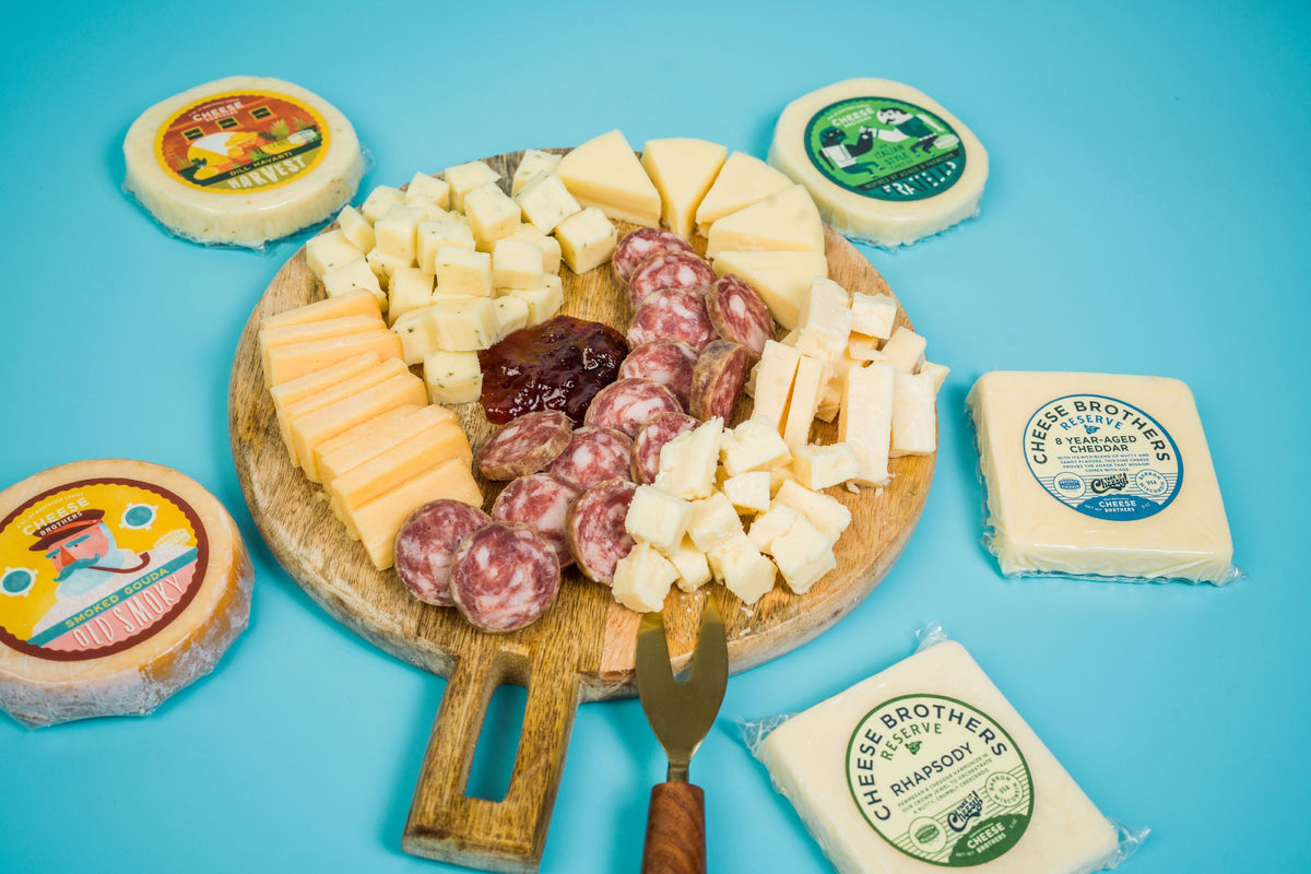 Charcuterie board with a variety of artisan Wisconsin cheeses, curds, sausages and mustard surrounded by packages. 