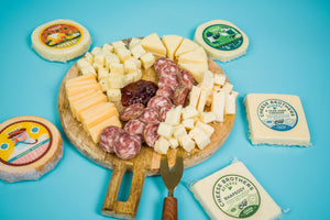 Charcuterie board with a variety of artisan Wisconsin cheeses, curds, sausages and mustard surrounded by packages. 