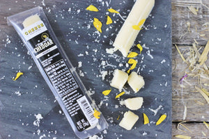 Package of gourmet cheddar cheese stick on a black slate.