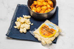 Package of cheese curds, a bowl fried curds, and cheese curd on black cloth.