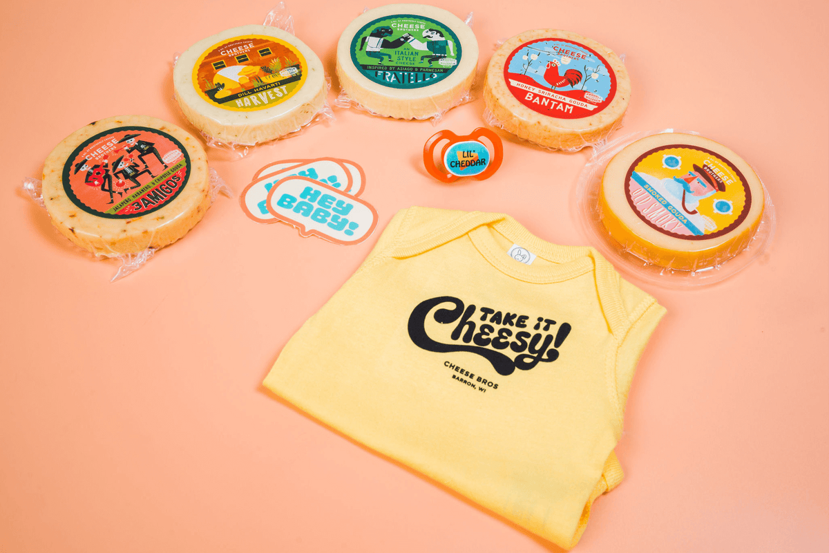 Five varieties of artisan cheese packages, stickers, a pacifier, and a Cheese Brothers baby onesie. 