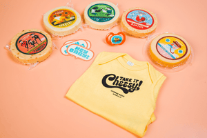 Five varieties of artisan cheese packages, stickers, a pacifier, and a Cheese Brothers baby onesie. 