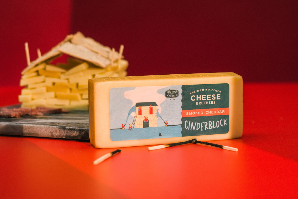 Package of Cinderblock gourmet smoked Wisconsin cheddar next to burnt matches and cheese house. 