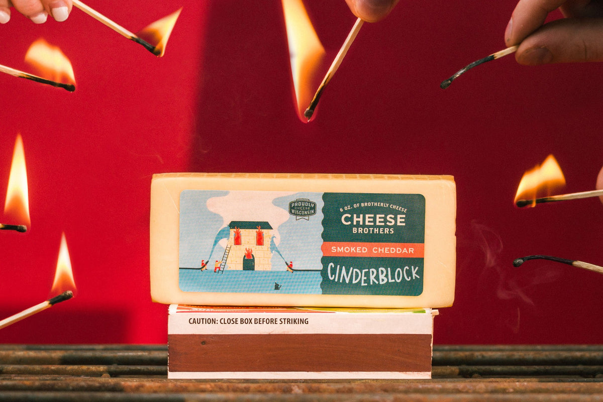 Package of Cheese Brothers cinderblock smoked cheddar cheese surrounded by lit matches. 