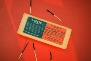 Package of Cheese Brothers cinderblock smoked cheddar cheese surrounded by lit matches. 