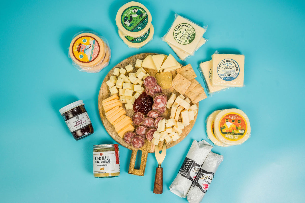 Deluxe charcuterie board with ten packages of artisan cheeses, jam, salamis, and mustard. 