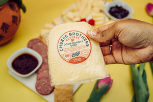 Hand holding a package of door county duet gouda parmesan cheese above charcuterie board. 