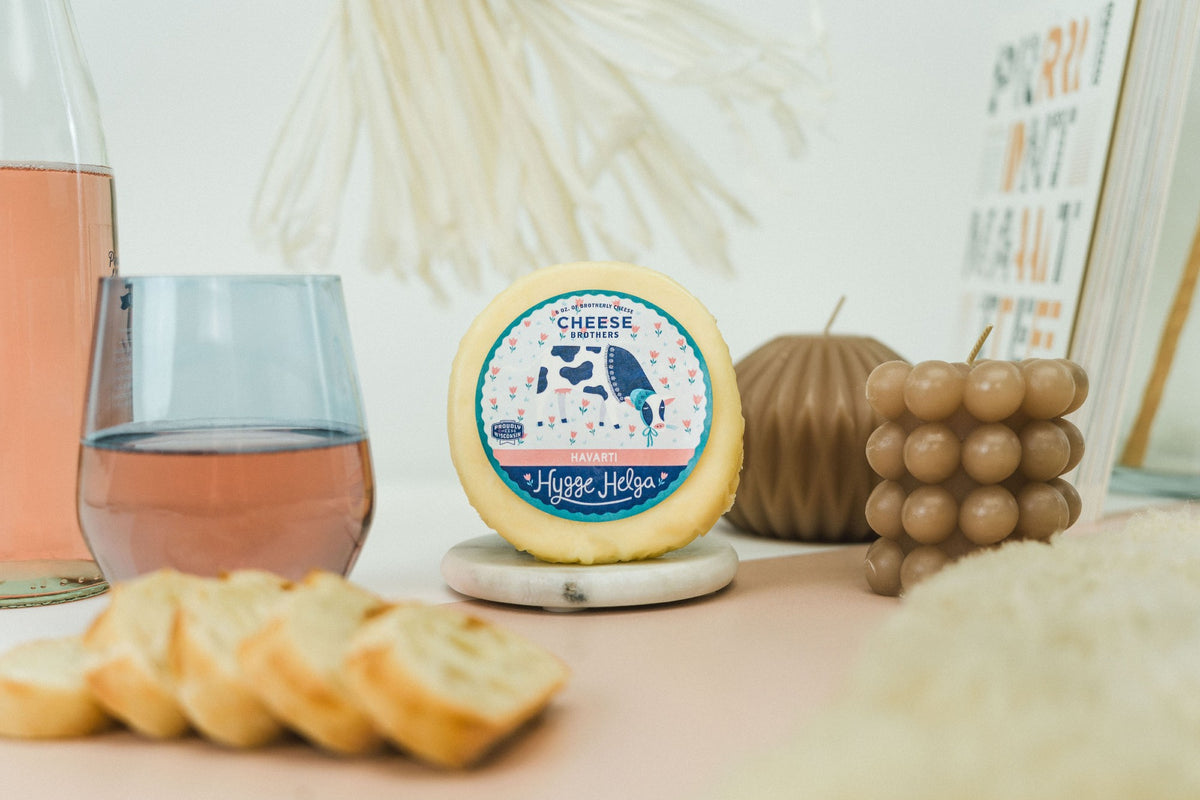 Package of artisan havarti next to bread slices, books, and a glass of wine. 
