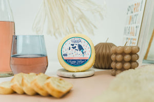 Package of artisan havarti next to bread slices, books, and a glass of wine. 