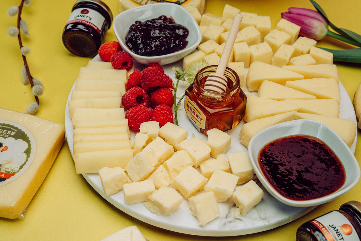 Mother&#39;s Day charcuterie board with a variety of gourmet cheeses, berries, jam, and honey. 