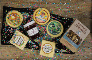 Aerial view of the contents of retirement gift box with five varieties of gourmet cheese, organic crackers, and jam. 
