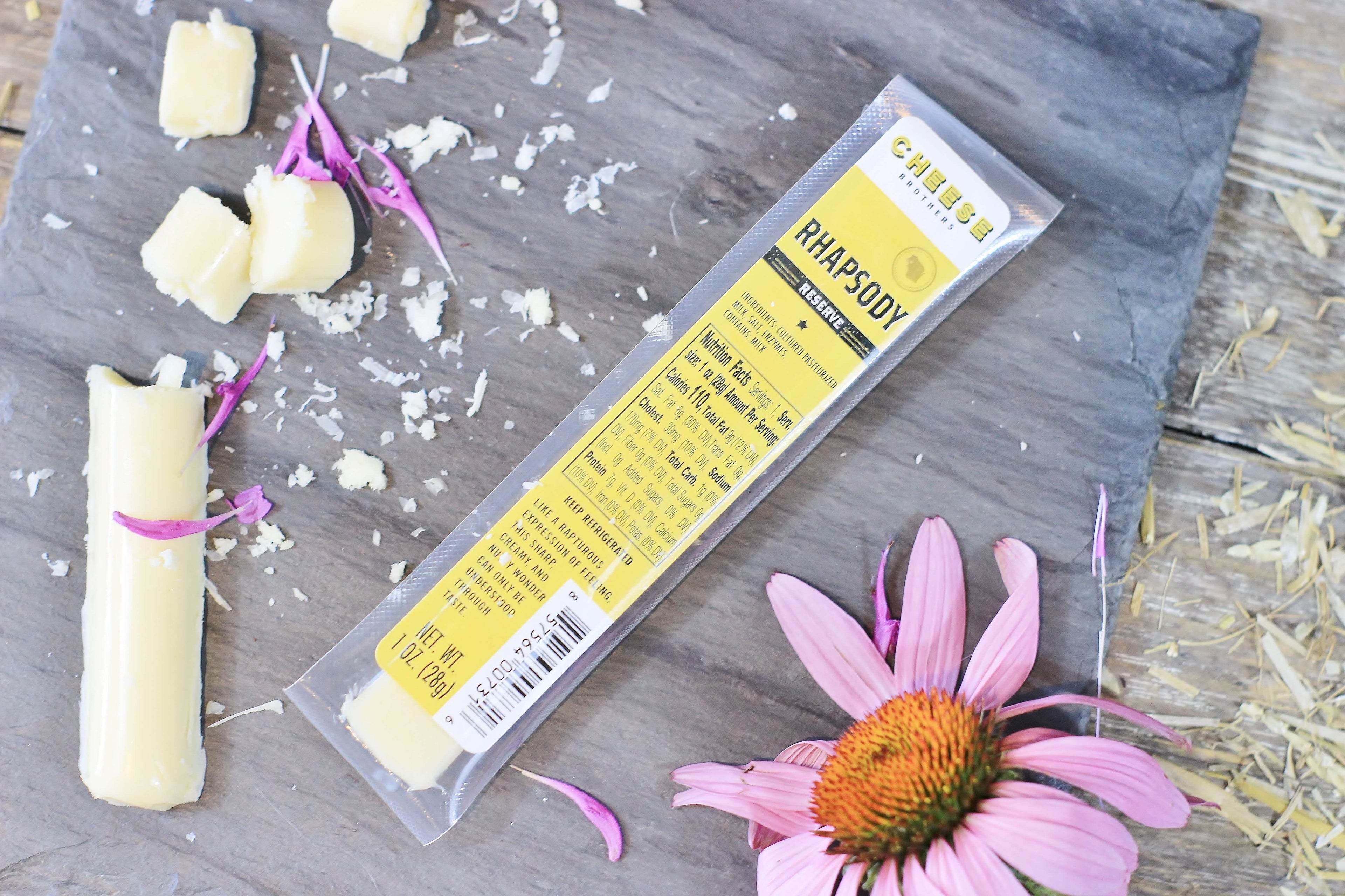 Rhapsody gourmet cheese sticks in and outside the package on a black slate with pink flower.