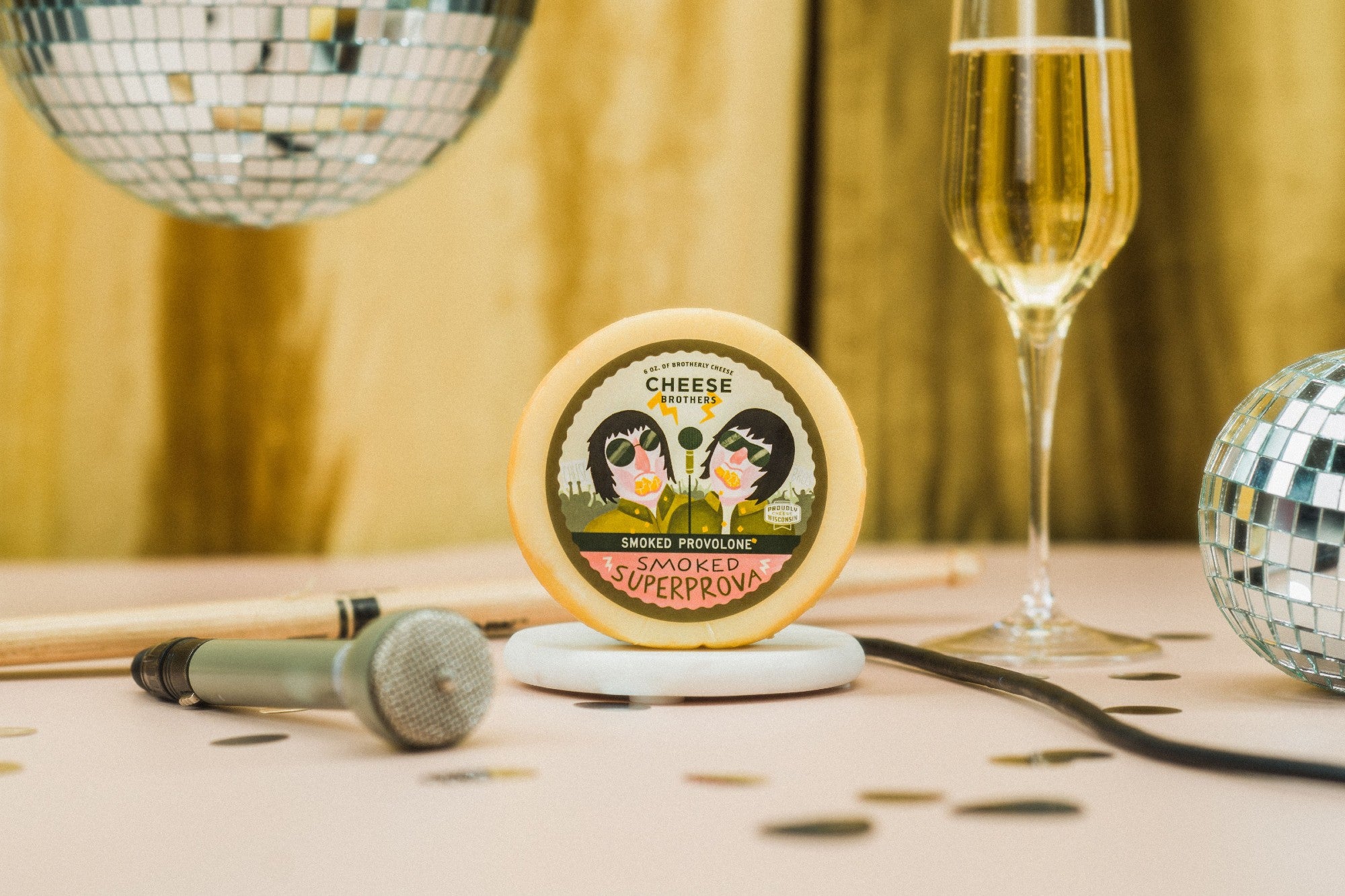 Package of artisan smoked provolone next to microphone, champagne, and disco balls. 