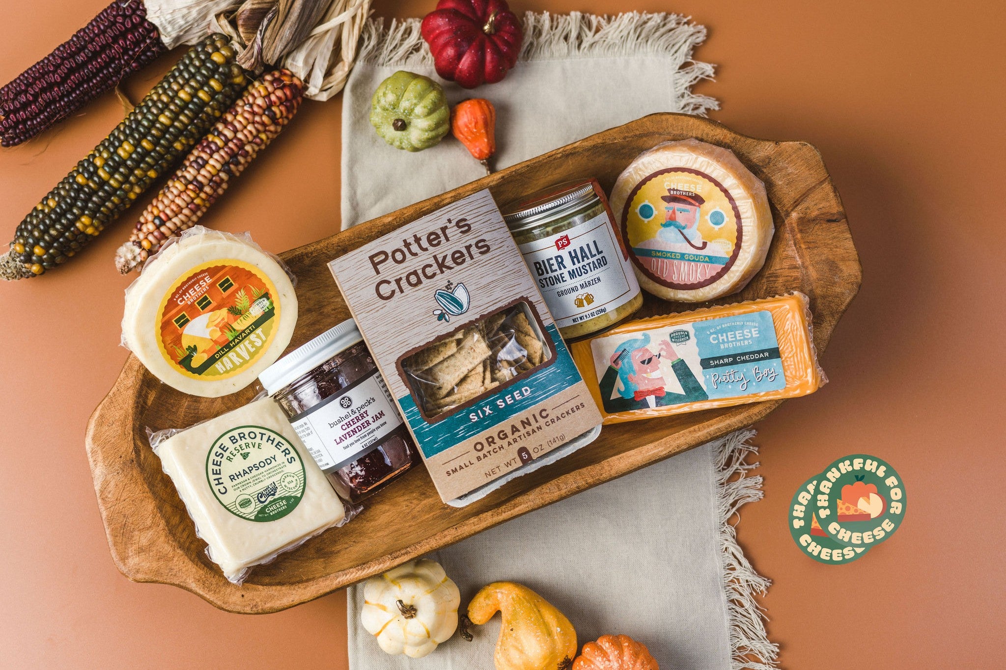 Thanksgiving cheese box with a variety of cheeses, jam, mustard, and crackers in a fall display. 
