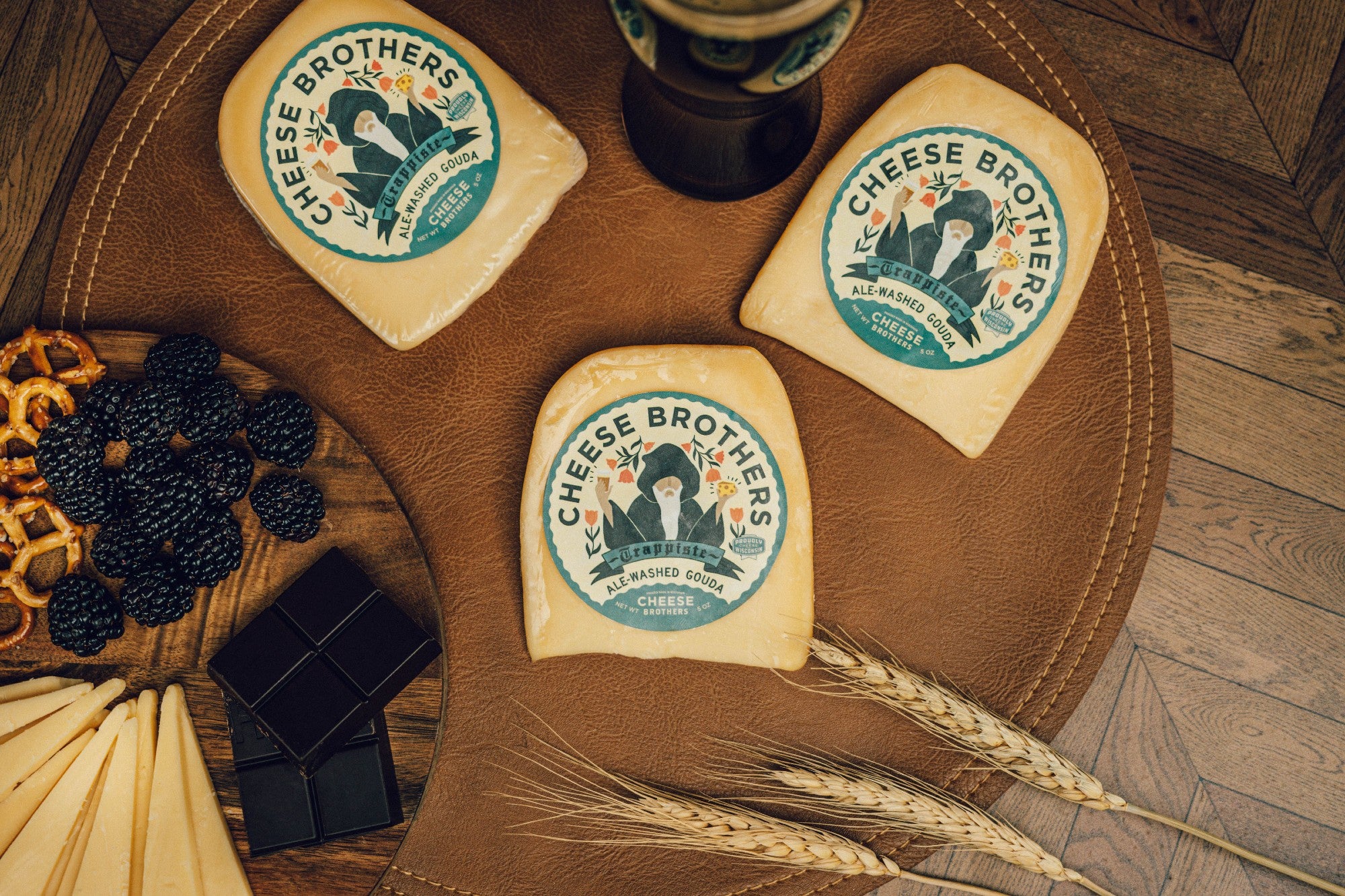 Package of ale-washed gouda on a plate with berries, pretzels, cheese slices, and chocolate. 