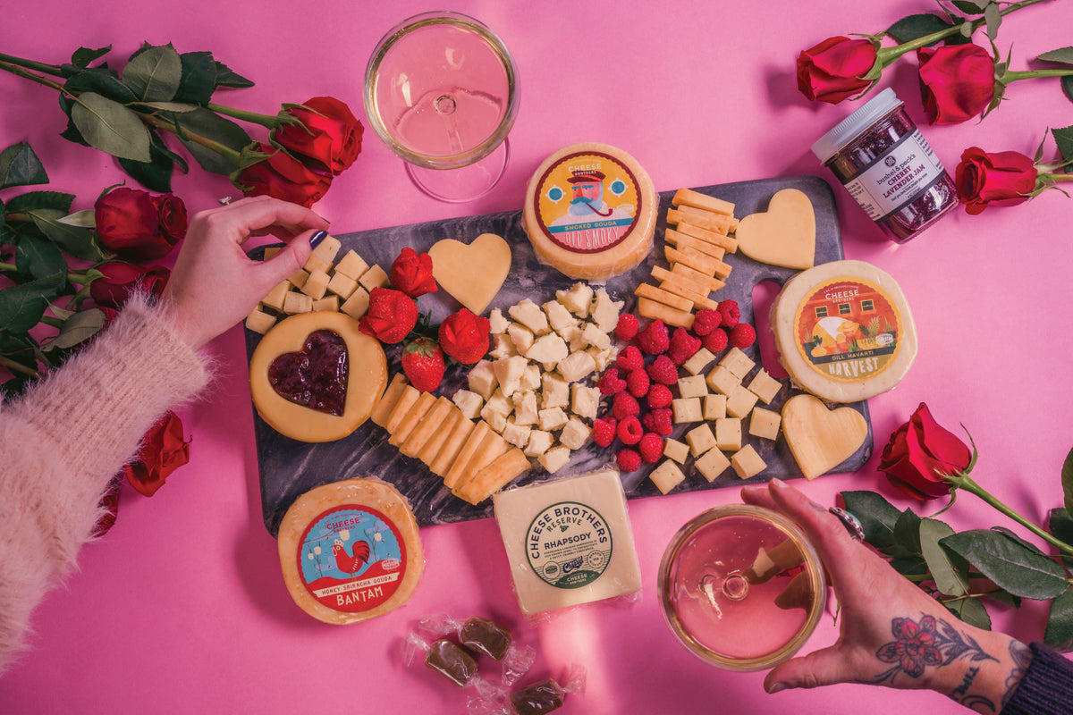 Hands picking from a black charcuterie board with packages of gourmet cheeses and caramel bites. 