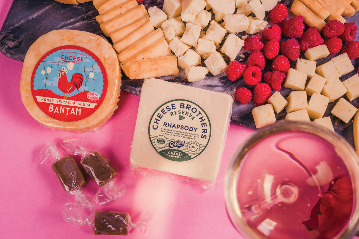 Black charcuterie board with packages of gourmet cheeses and caramel bites. 